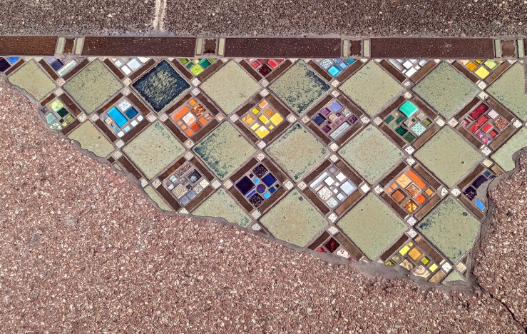 Close-up of a colorful tile mosaic patch embedded in a sidewalk, featuring a diamond pattern with various shades and shapes.