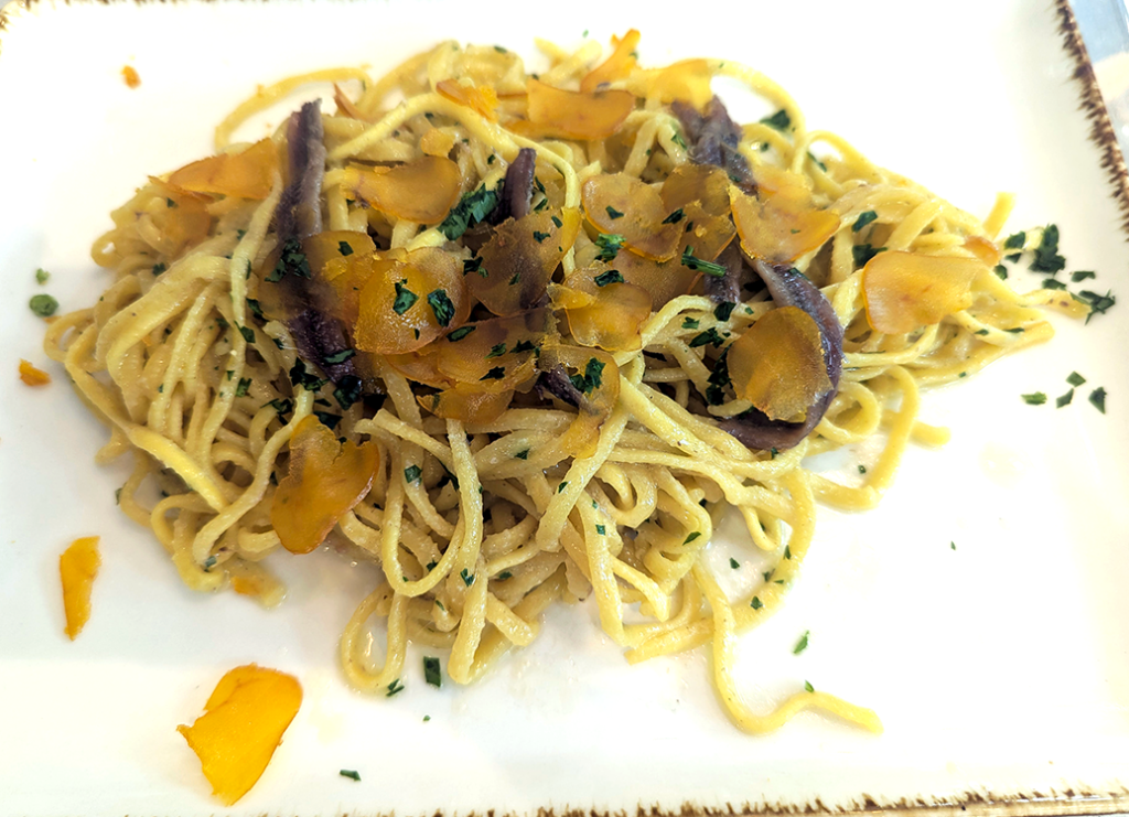 Plate of pasta topped with herbs and thinly sliced yellow vegetables