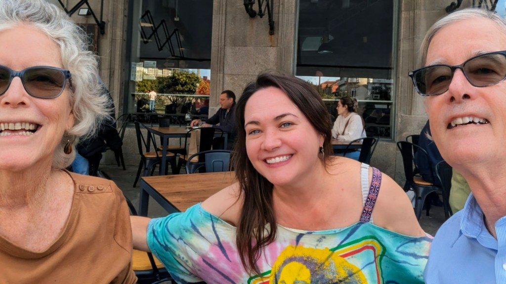Three people smiling for a selfie in a café setting, with tables and chairs in the background.
