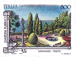 An Italian postage stamp featuring a scenic view of the Miramare Gardens in Trieste, showcasing neatly trimmed hedges, a statue, and a fountain against a background of trees and the sea.