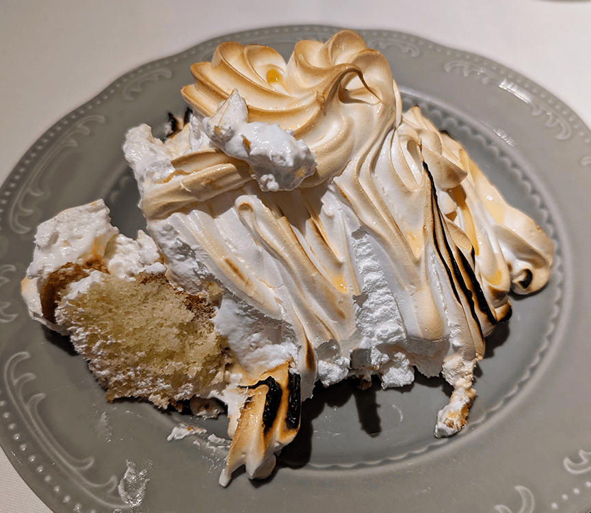 A slice of layered cake topped with fluffy meringue, showing its golden-brown toasted peaks on a decorative plate.